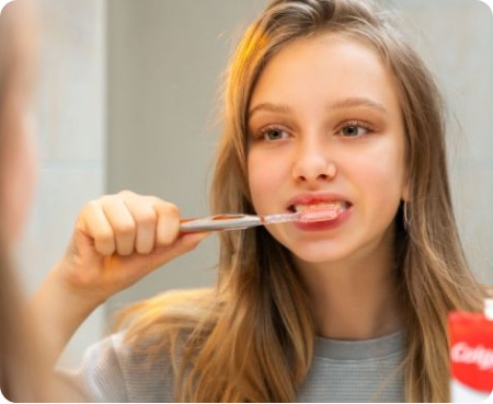 Une fillette se brossant les dents devant un miroir dans le cadre d'une bonne hygiène bucco-dentaire.