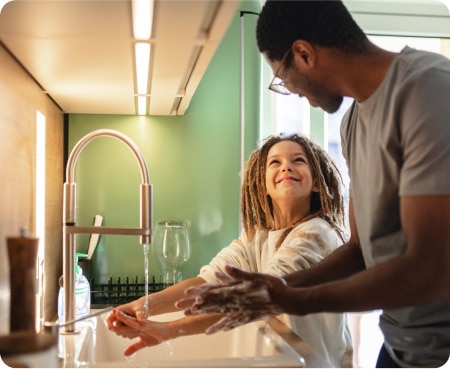 Un homme devant un évier de cuisine montre à un enfant comment se laver les mains correctement dans le cadre d'une bonne hygiène personnelle.